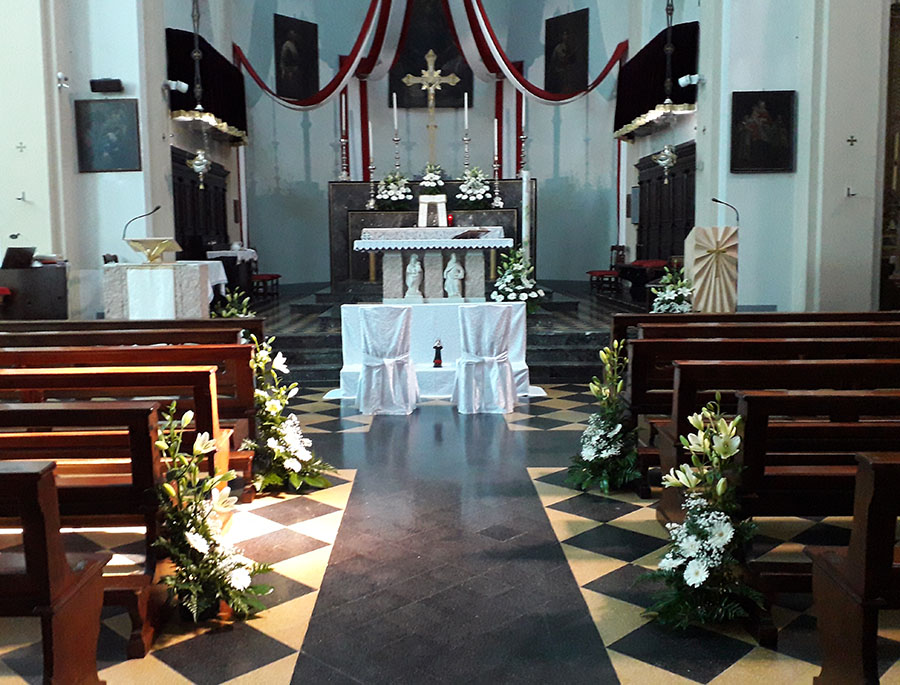 L'interno di una chiesa addobbata per un matrimonio con ciotole di diverso formato compsote da lilium bianchi e margherite con velo da sposa e foglie verdi