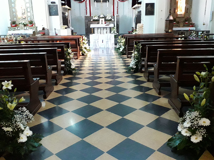 la navata della chiesa di zogno con i banchi addobbati di composizione di gigli e rose bianche e  bianchi