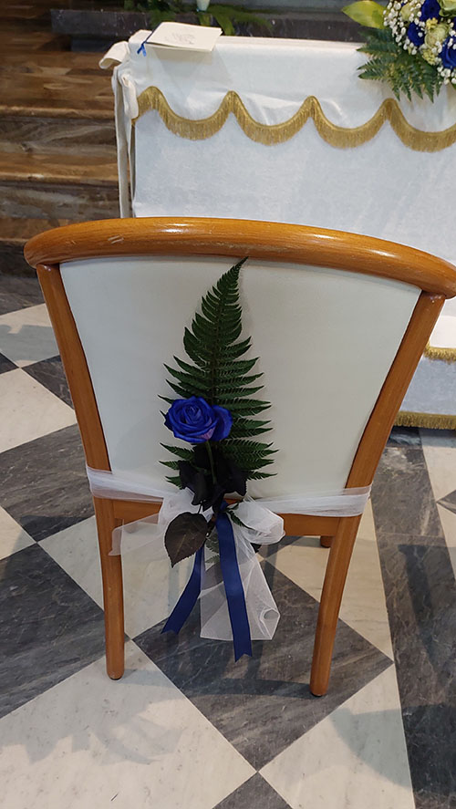 Sedia in chiesa addobbata per la sposa con una rosa blu e una felce verde agganciata alla sedia con un fiocco di tulle color bianco e un nastro blu