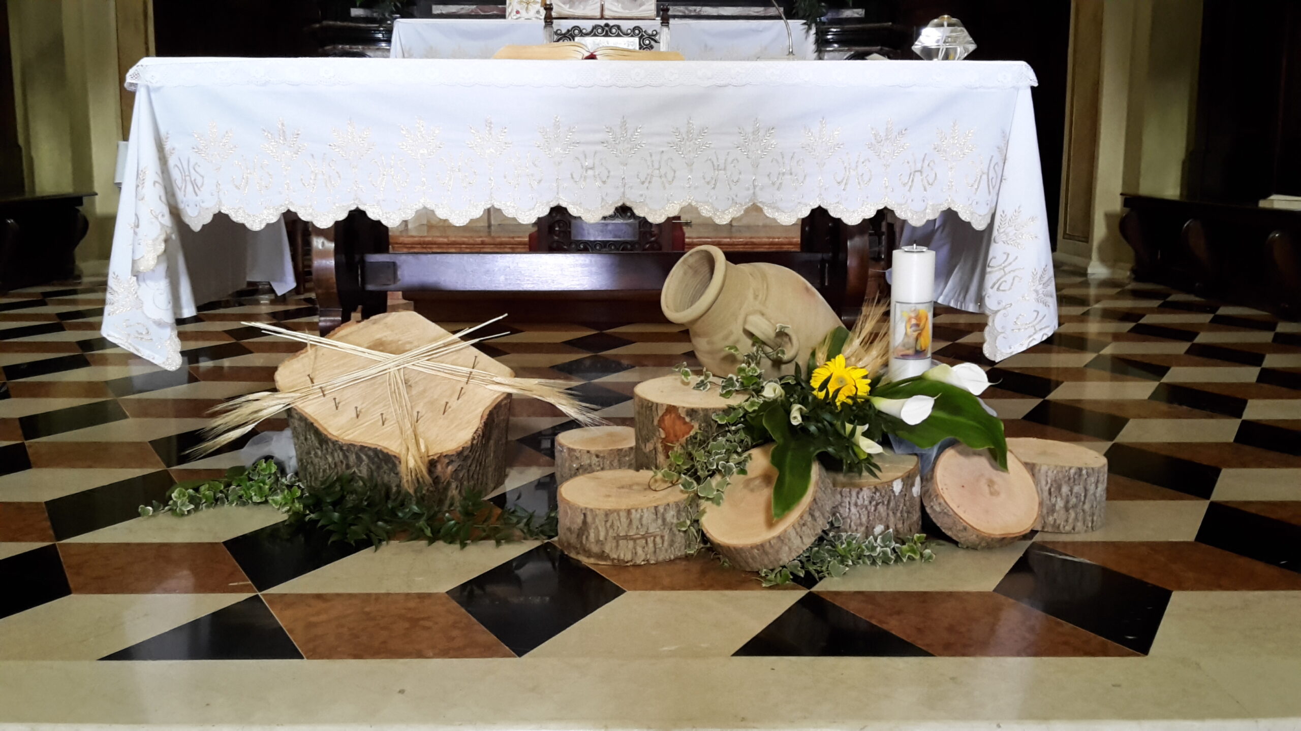 composizione di tronchi di legno e anfore con  margherite gialle e candela posizionati sulla base di un altare