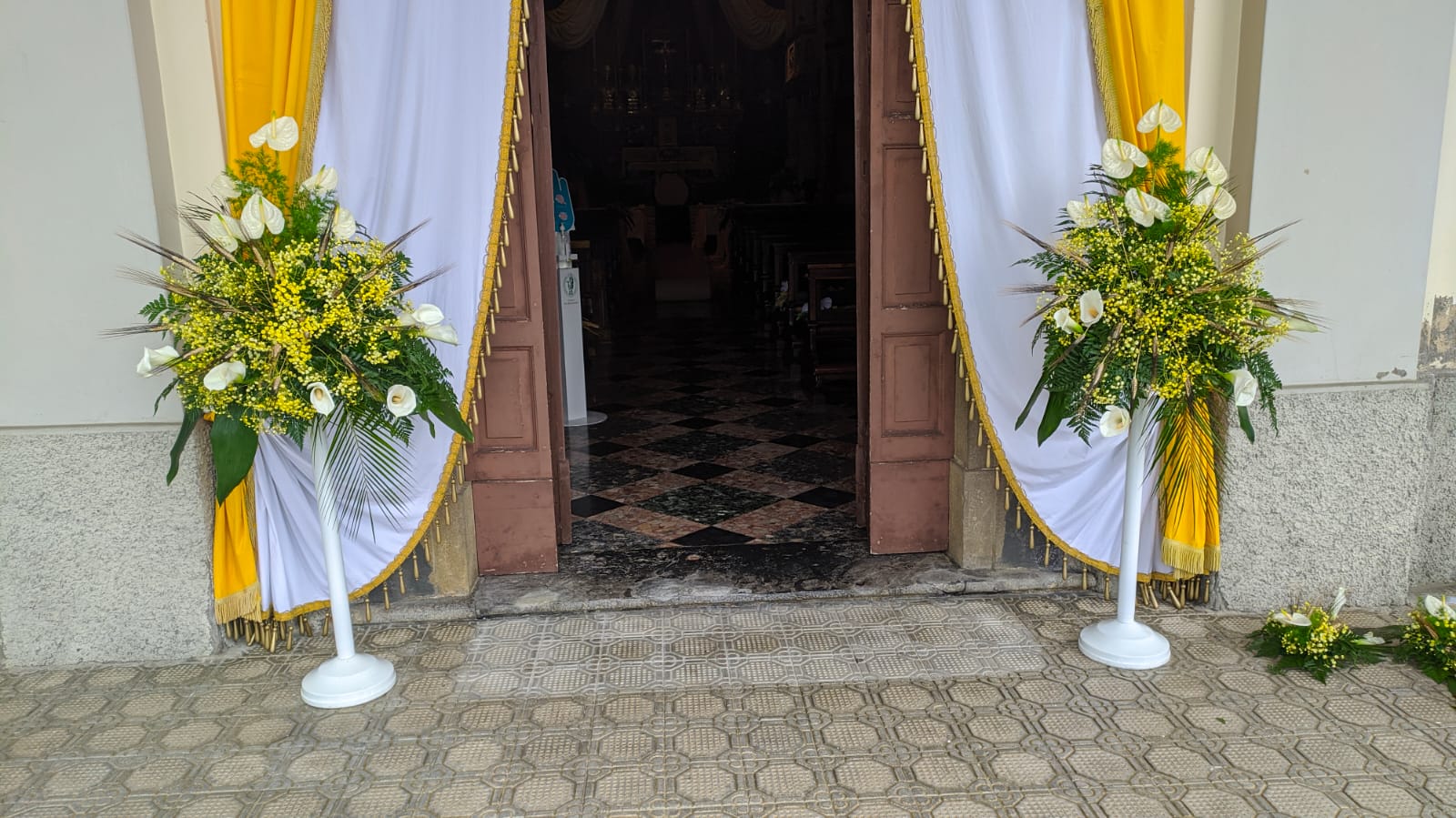 Cestini composizioni florali con calle bianche e mimosa su piedistalli bianci all'ingresso di una chiesa