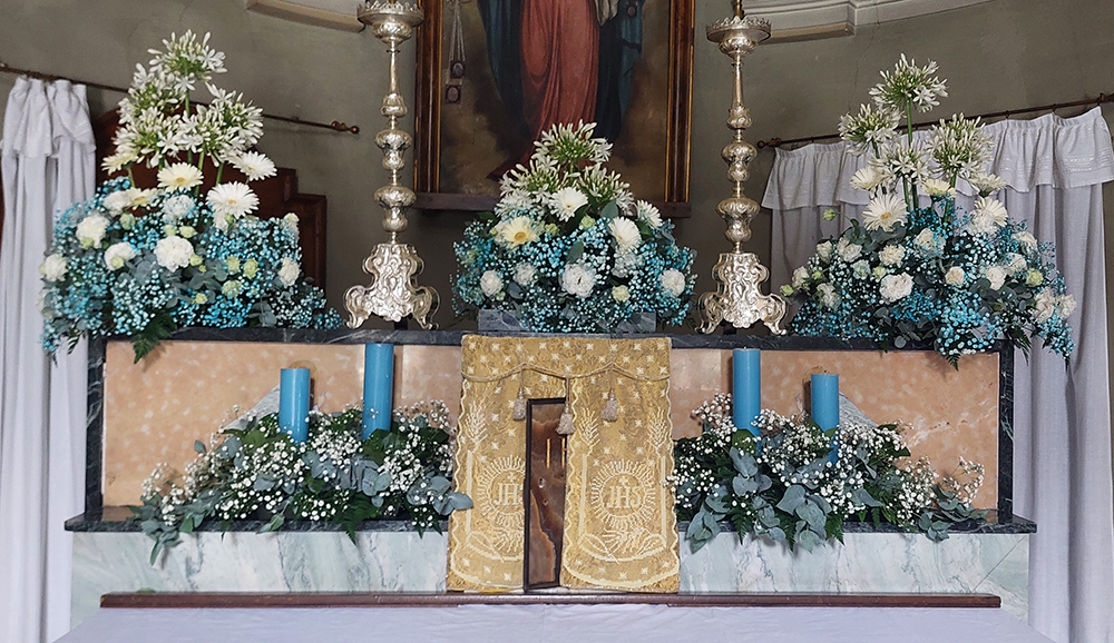 Altare addobbato con composizioni di margherite bianche e rose bianche velo da sposa bianco e azzurro foglie versi e azzurre candele azzurre 