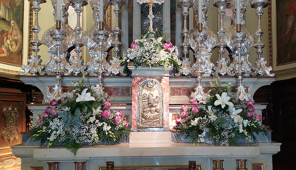 Addobbi sull'altare di una chiesa composti da composizioni floreali con ciotole di rose  bianche con bordo fucsia, lilium bianchi velo da sposa e fiori  a grappolo bianchi