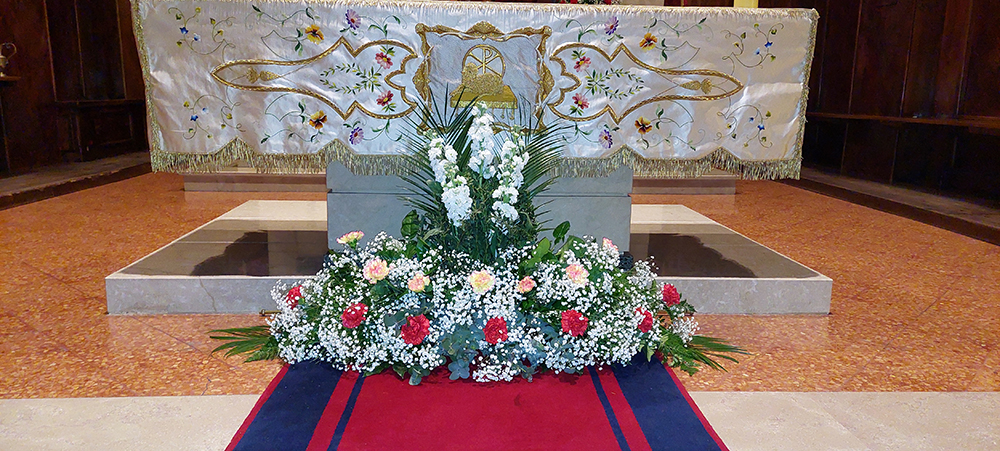Addobbo floreale alla base di un altare di una chiesa composto da garofani rossi e garofani rosa econ velo da sposa e felci al centro tre fiori alti a grappolo bianchi